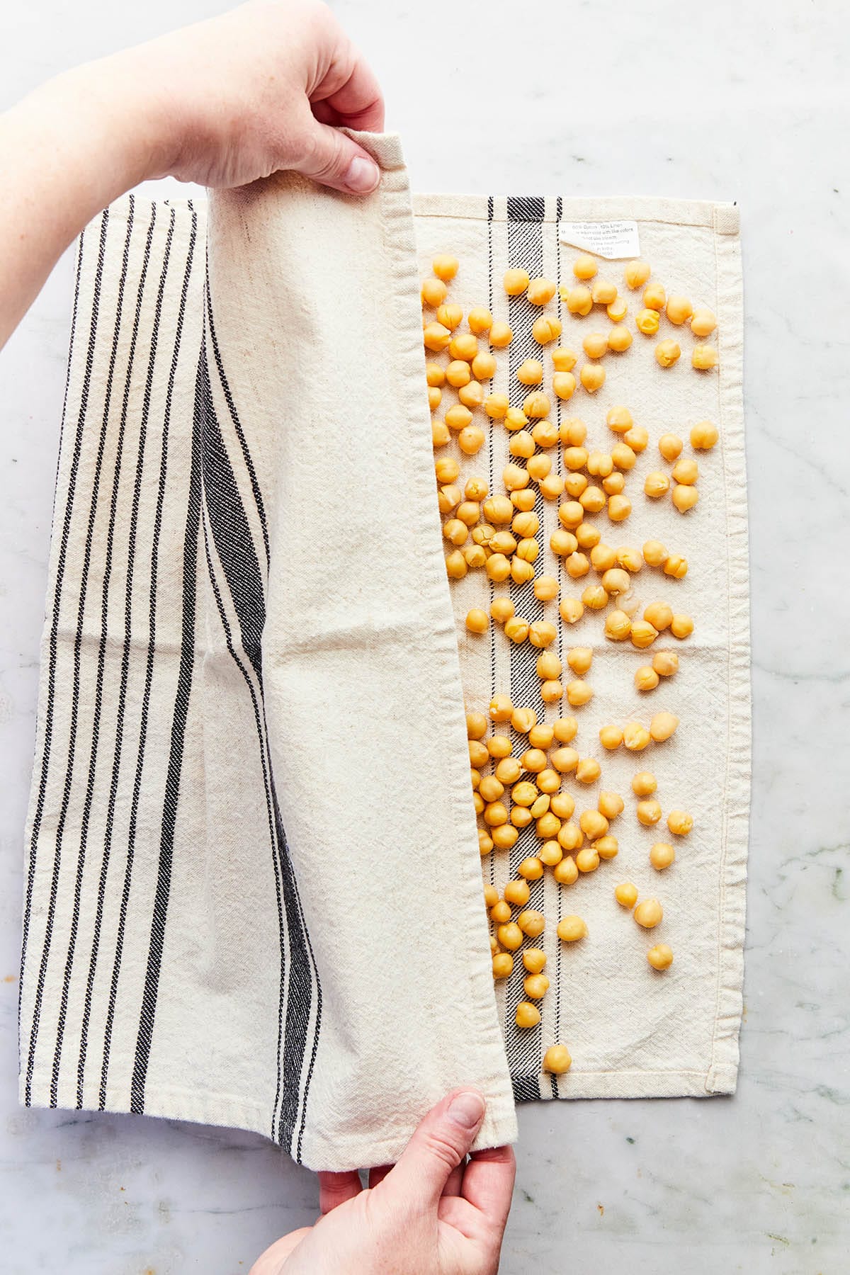 Hands covering chickpeas on a tea towel with the other half of the towel.