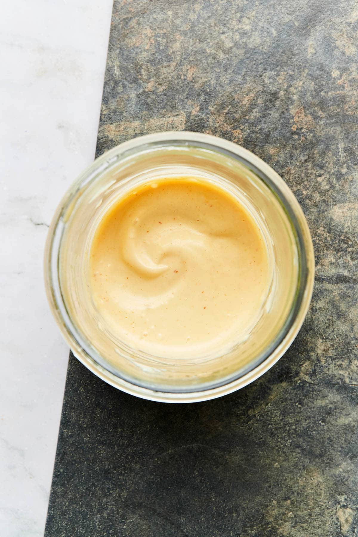 Overhead image of a jar of homemade spicy garlic aioli on a stone surface.
