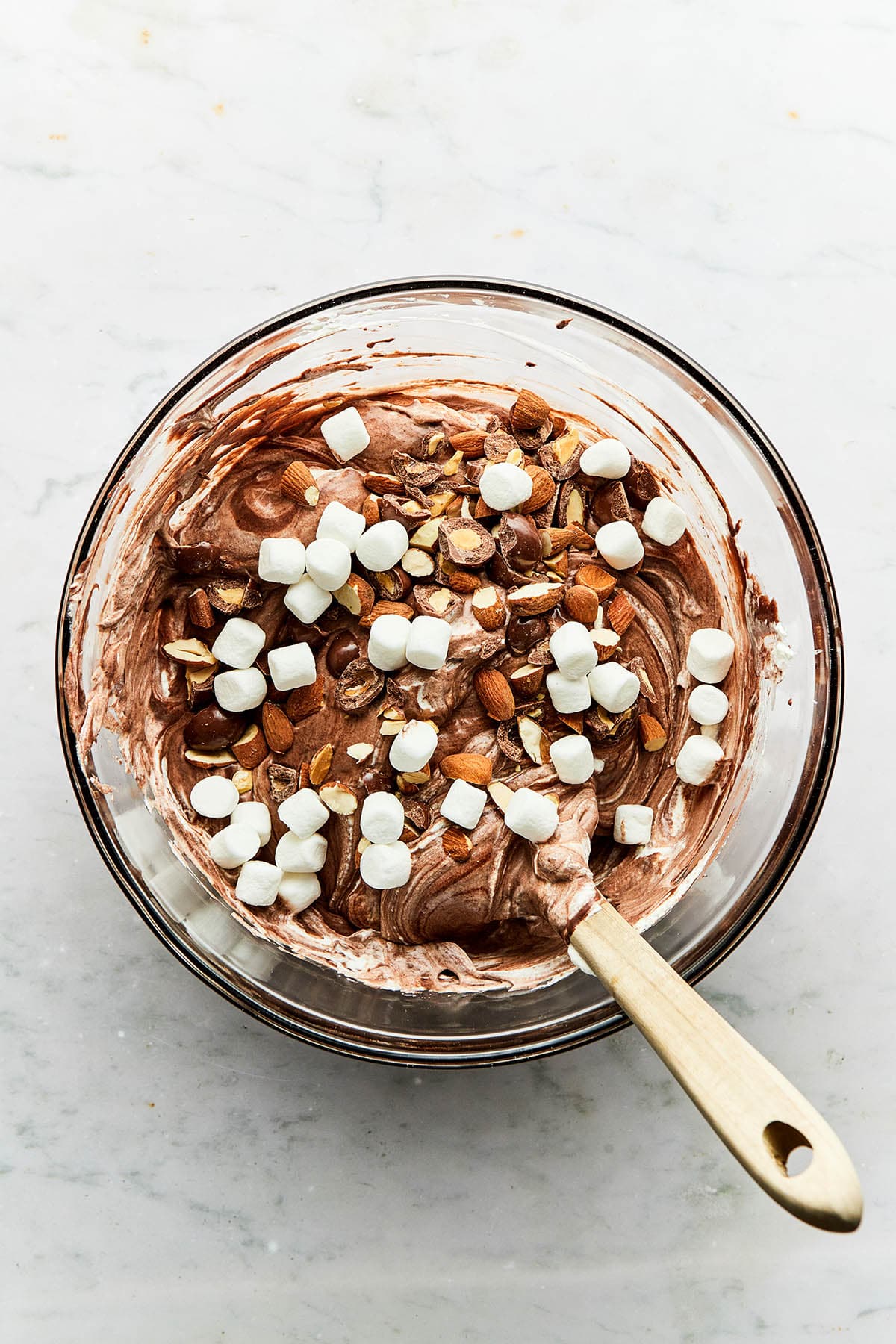 A bowl of fluffy chocolate batter topped with toasted almonds, chocolate covered almonds, and mini marshmallows.