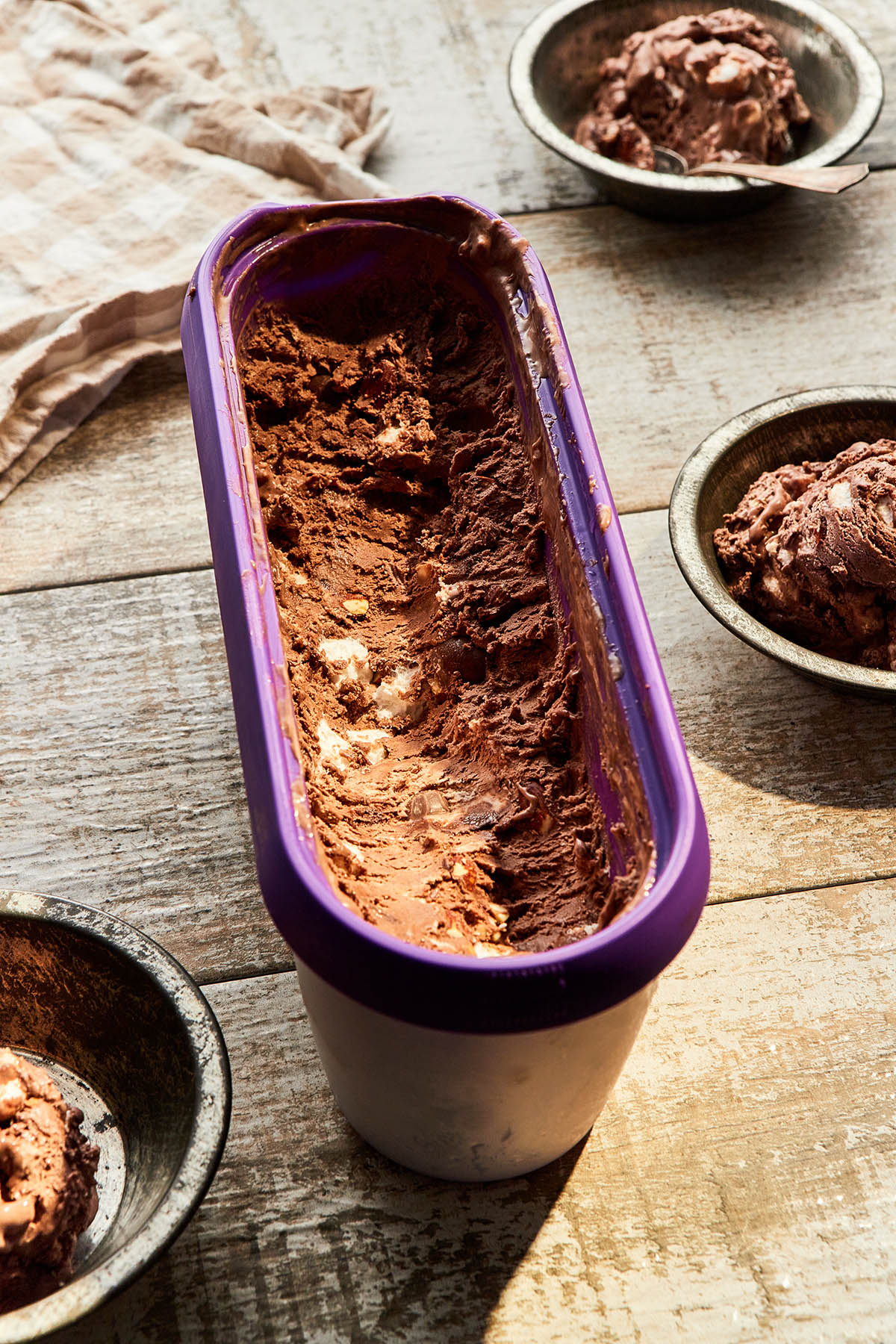 A long oval insulated ice cream tun of rocky road ice cream with half of the ice cream scooped out into dishes.
