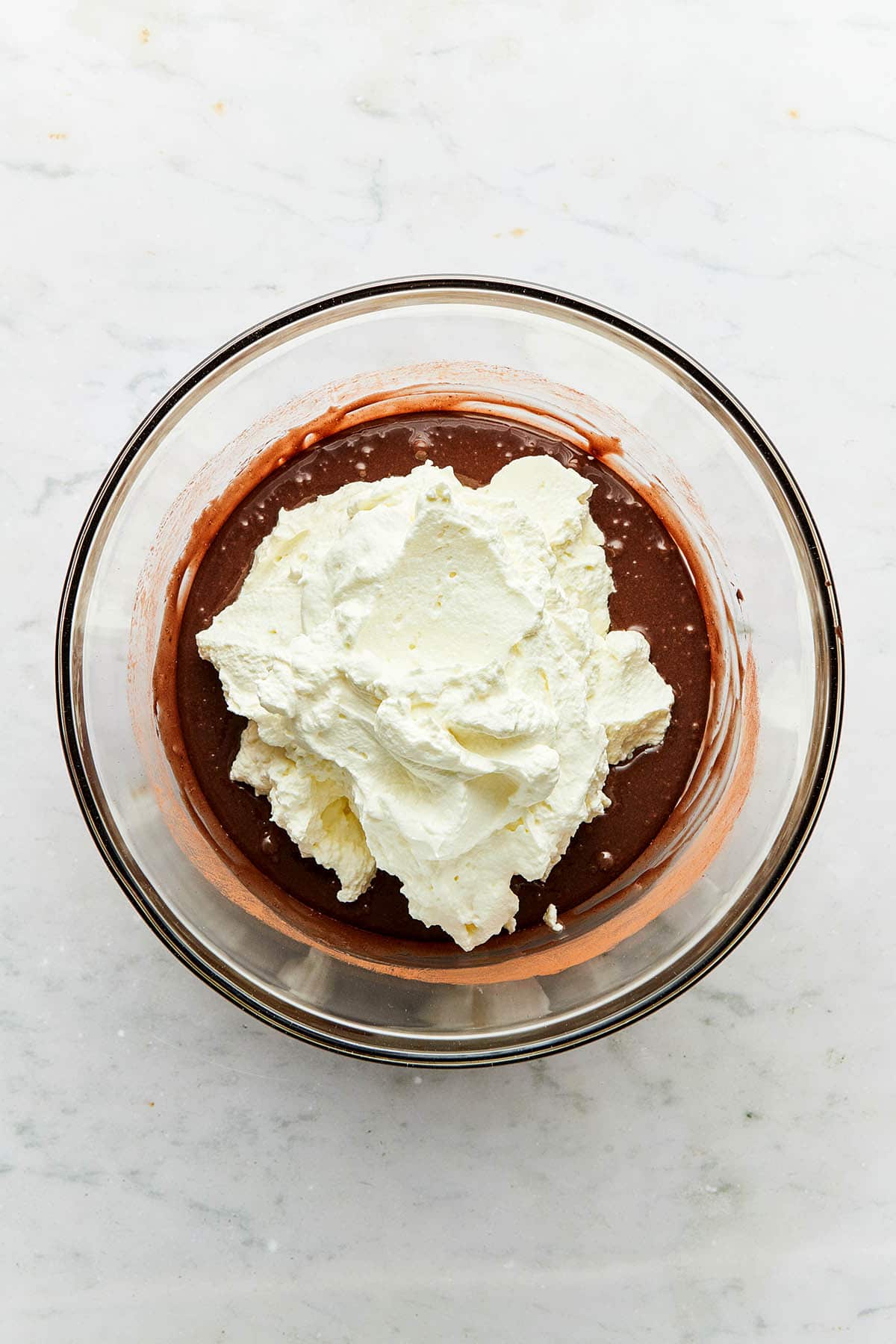 Whipped cream dolloped on top of chocolate batter in a glass bowl.