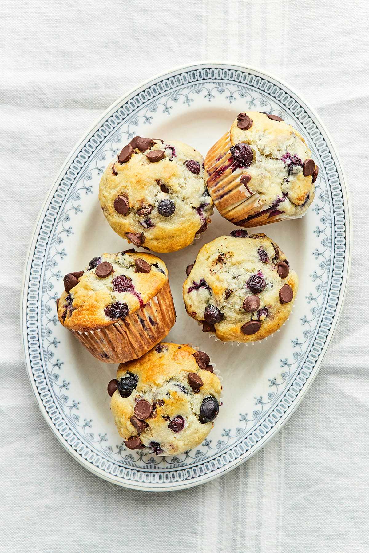 An oval platter of five blueberry chocolate chip muffins.