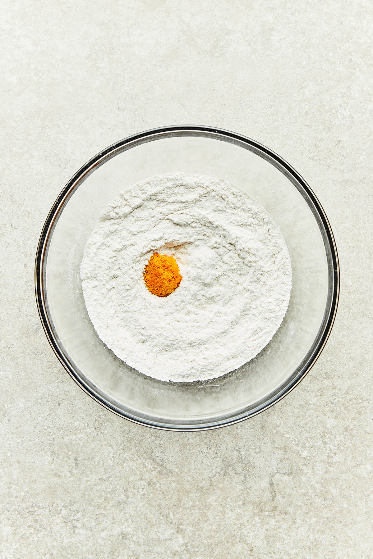 A bowl of unmixed flour, baking powder, salt, sugar, and grated orange zest.