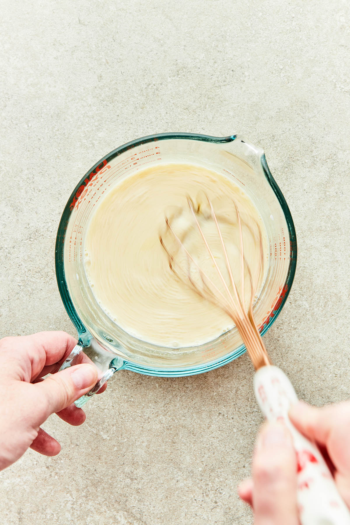A hand using a whisk to mix wet ingredients in a large measuring cup.