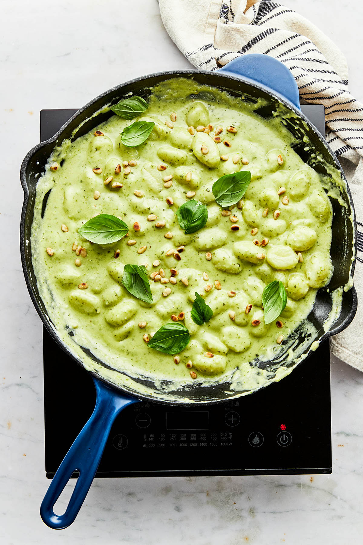 A pan of gnocchi pesto topped with toasted pine nuts and fresh basil leaves.