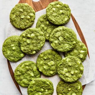 Matcha cookies laid on top of piece of parchment paper on a wooden teardrop-shaped board.