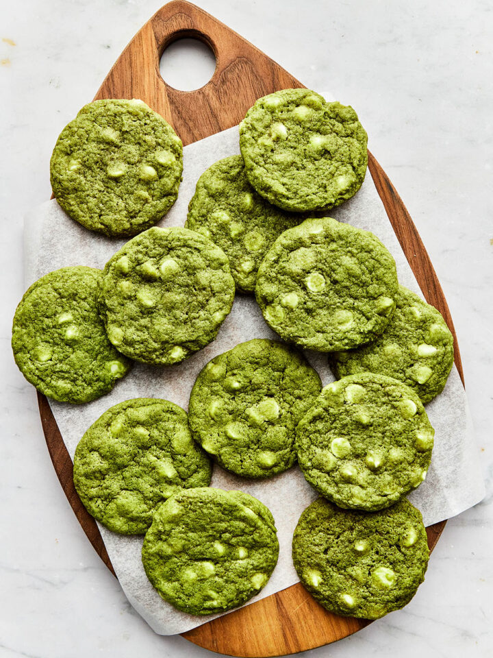 Matcha chocolate chip cookies laid on top of piece of parchment paper on a wooden teardrop-shaped board.