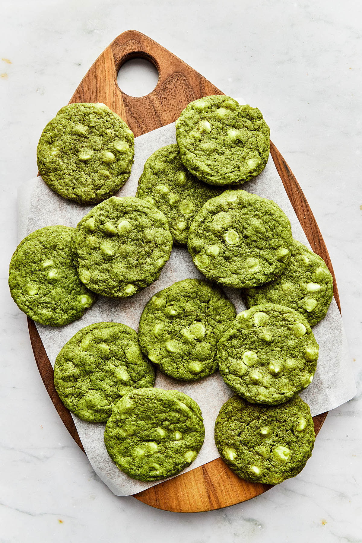 Matcha chocolate chip cookies laid on top of piece of parchment paper on a wooden teardrop-shaped board.