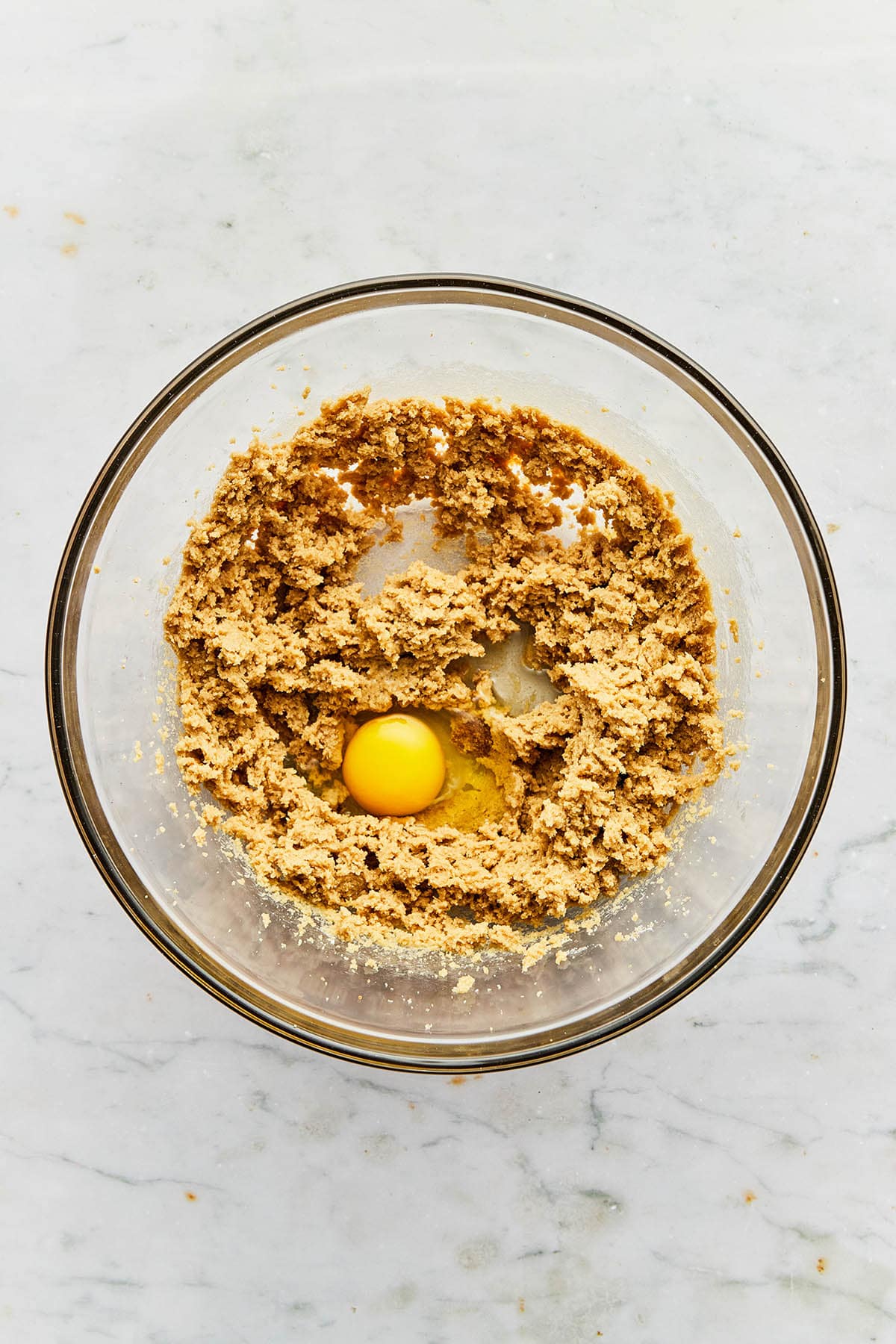 An egg in a bowl of mixed wet cookie ingredients.
