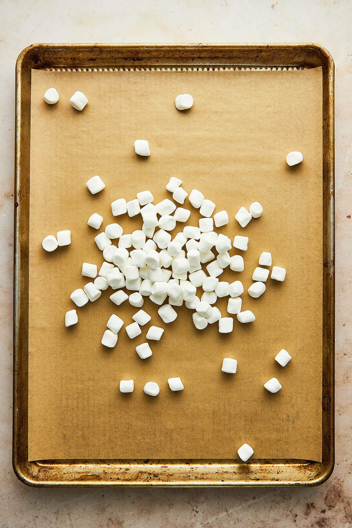 Mini marshmallows in a pile on a baking sheet lined with parchment paper.