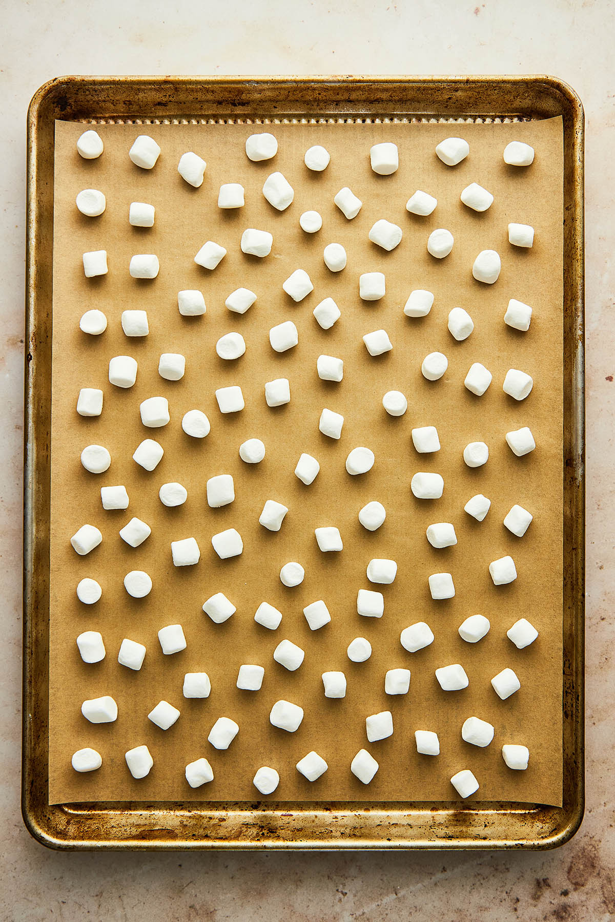 Mini marshmallows spread evenly across a baking sheet lined with parchment paper. None of the marshmallows are touching.