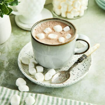 A mug of how chocolate topped with dehydrated marshmallows on a kitchen counter.