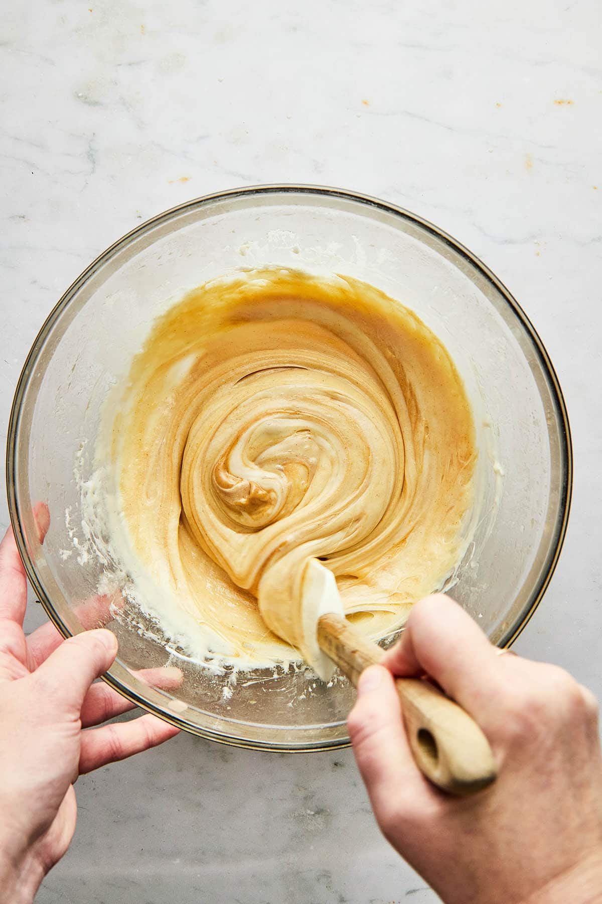 A hand using a rubber spatula to stir melted marshmallow and peanut butter together.