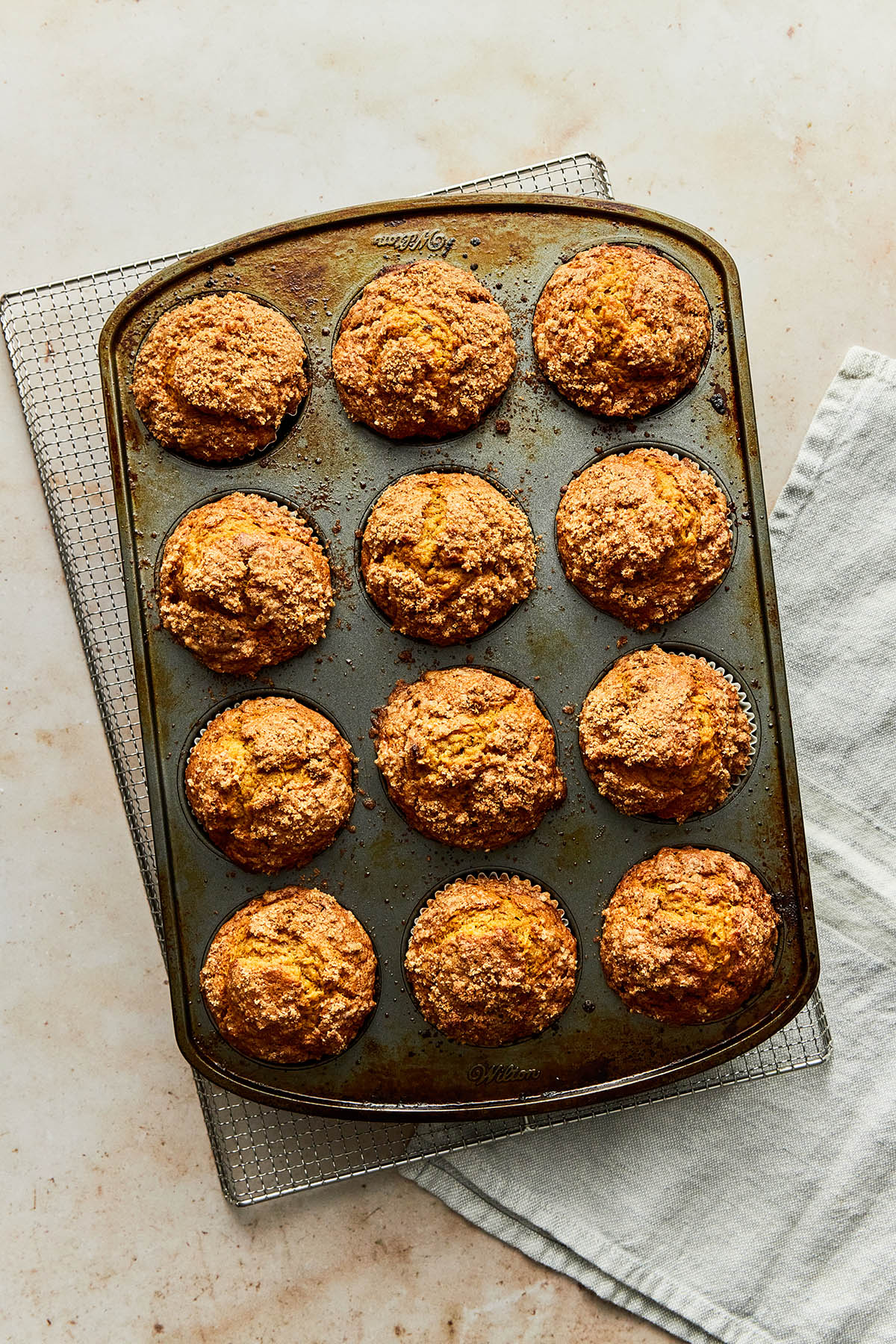 A pan of pumpkin banana muffins on a wire rack with a grey linen cloth underneath.