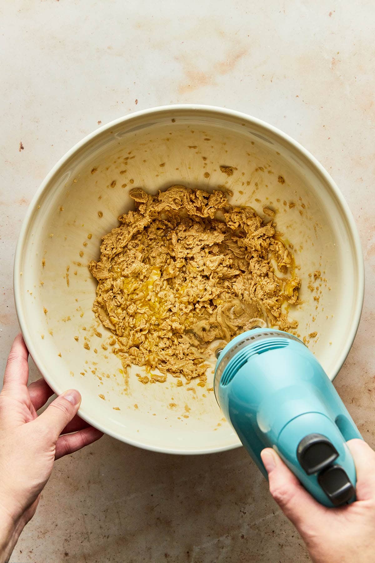 A hand using a hand mixer to mix an egg into wet muffin ingredients.