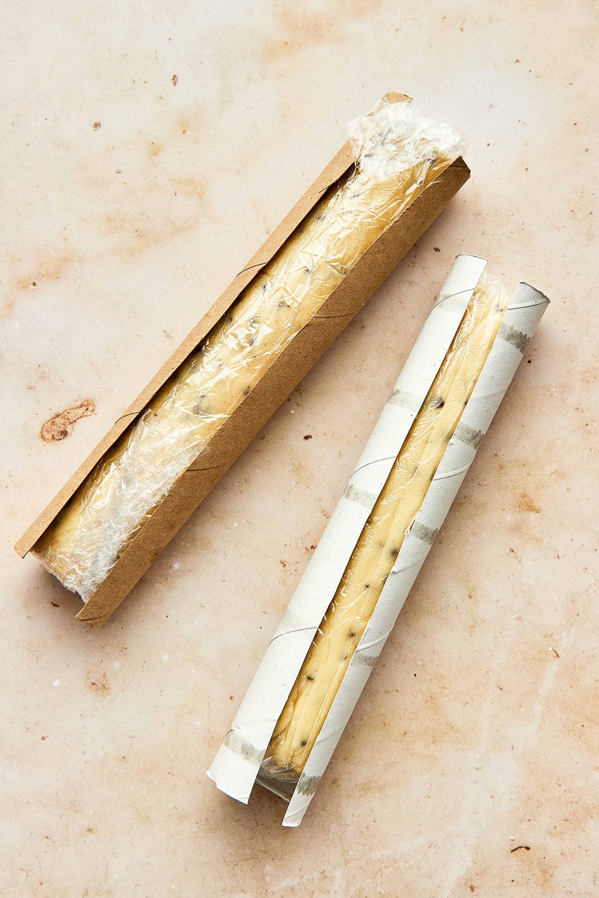 Logs of cookie dough rolled in plastic wrap and set into two cardboard paper towel tubes which have been cut down the length.