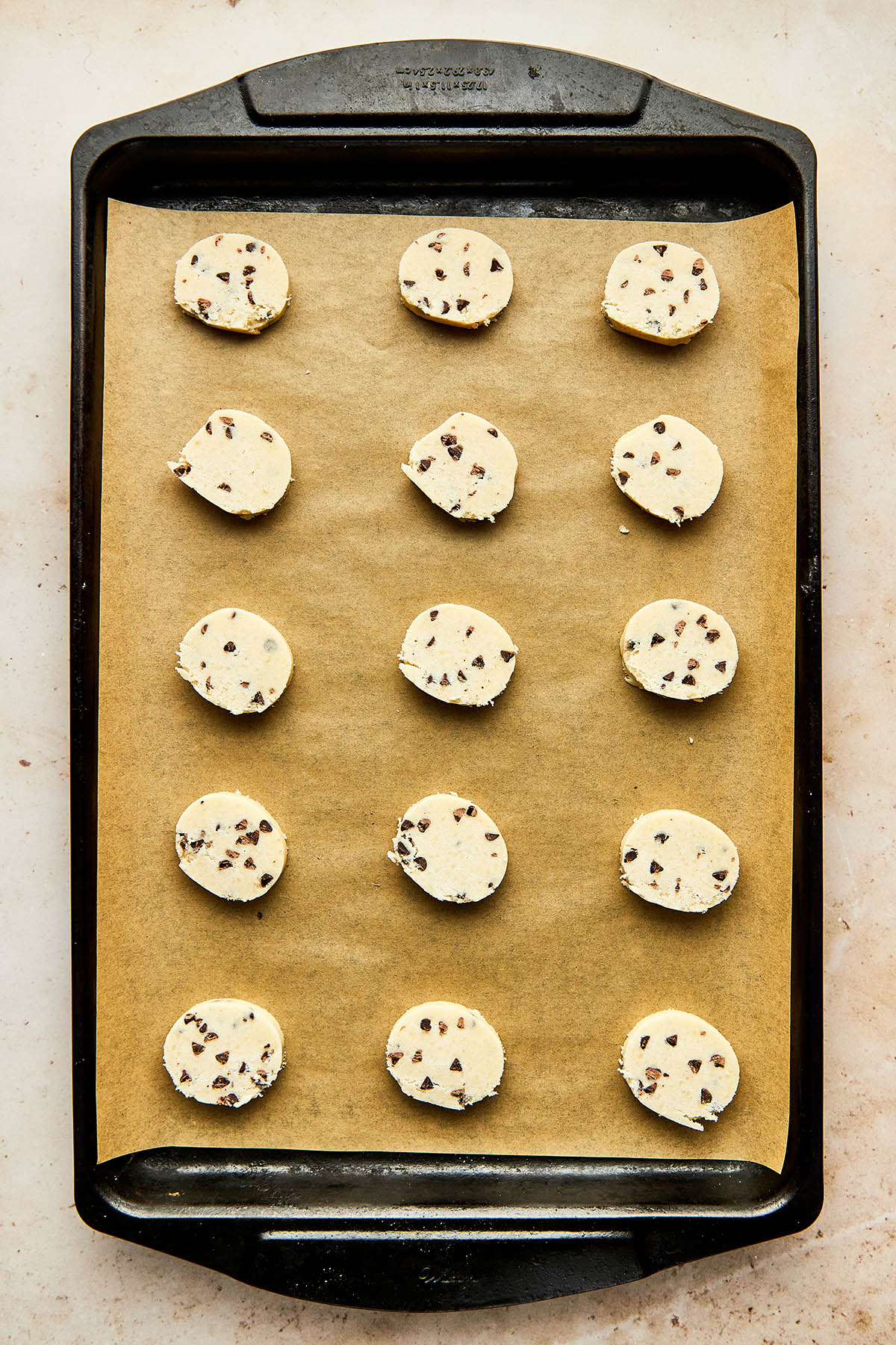 A baking sheet lined with kraft-coloured parchment paper topped with unbaked cookie slices.
