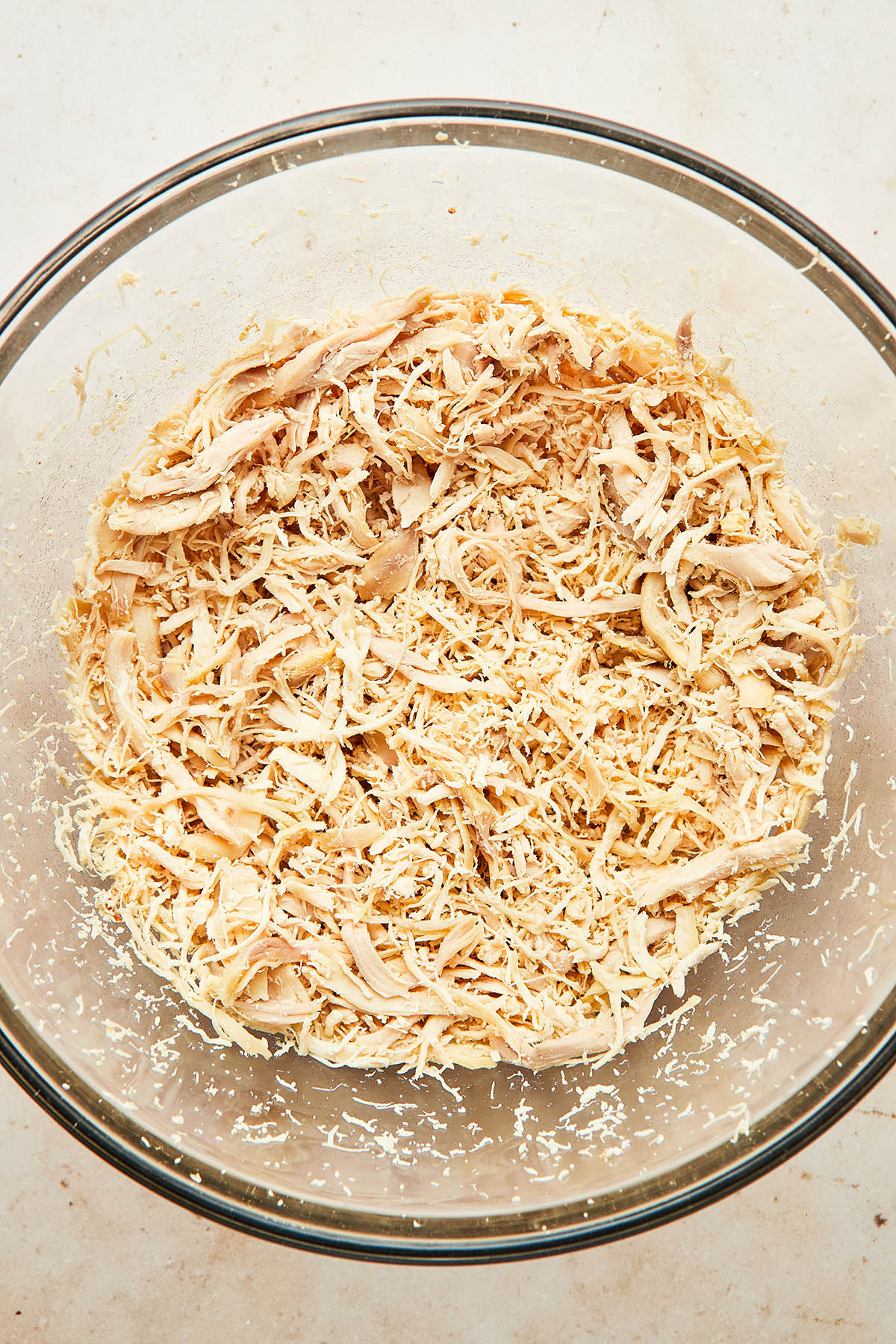A large glass mixing bowl of shredded chicken.
