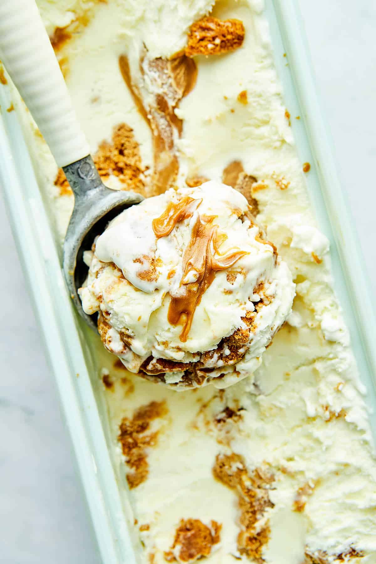 A scoop of Biscoff cookie butter ice cream in an ice cream scoop resting on top of a tub of oce cream.