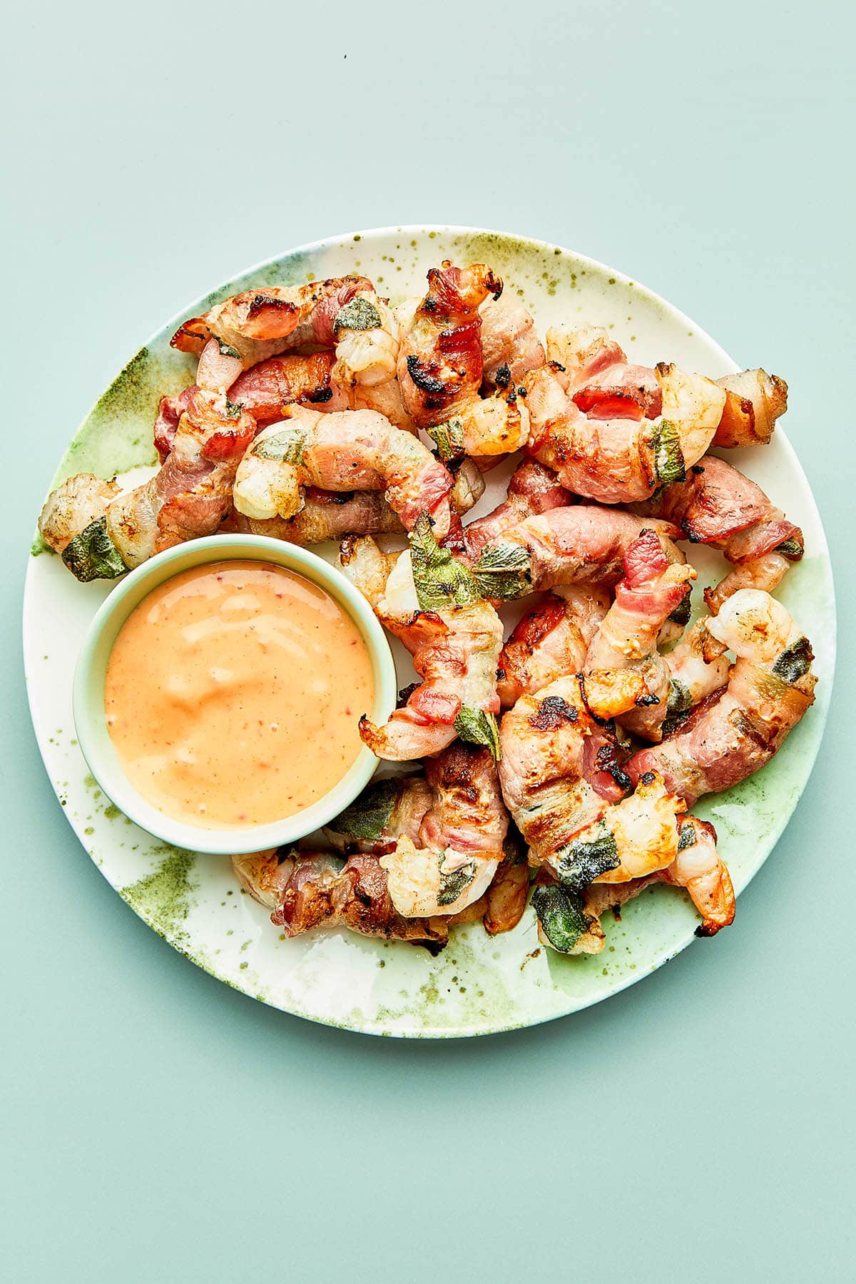 A plate of bacon wrapped shrimp on a plate with a small bowl of bang bang sauce.