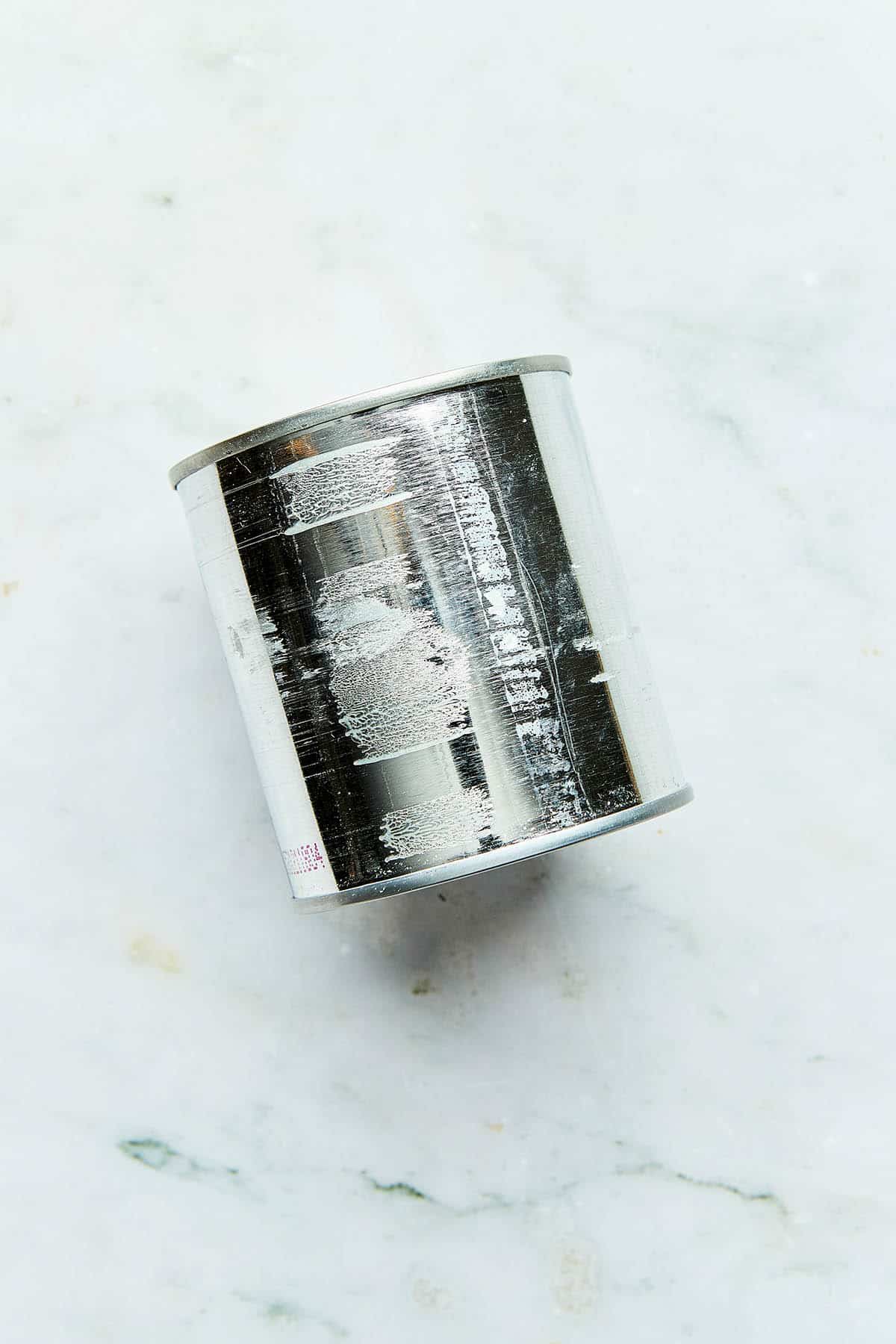 A small can with the label removed laying on a marble counter.