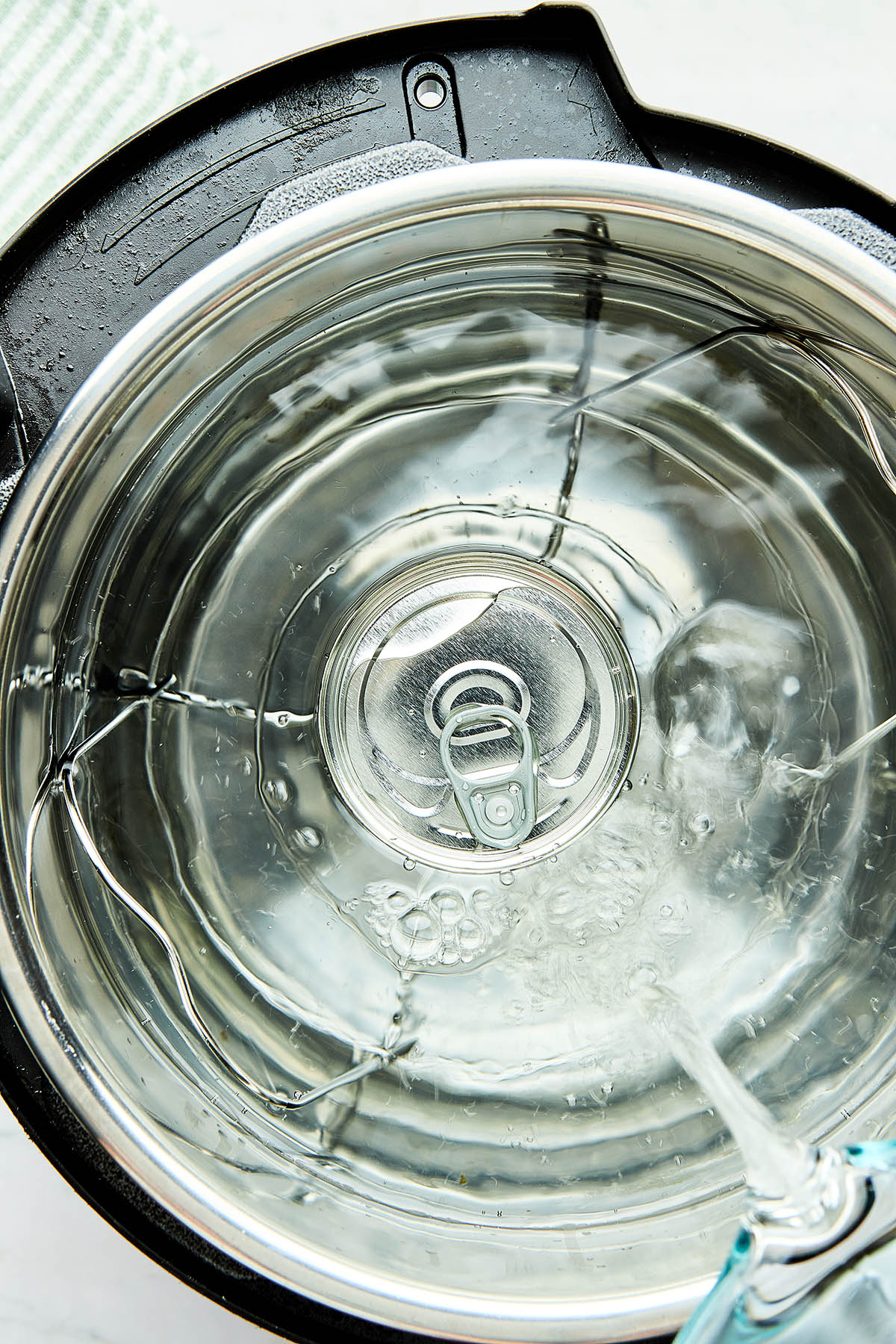 A small can standing inside an Instant pot as the pot is being filled with water from a glass Pyrex measuring cup.