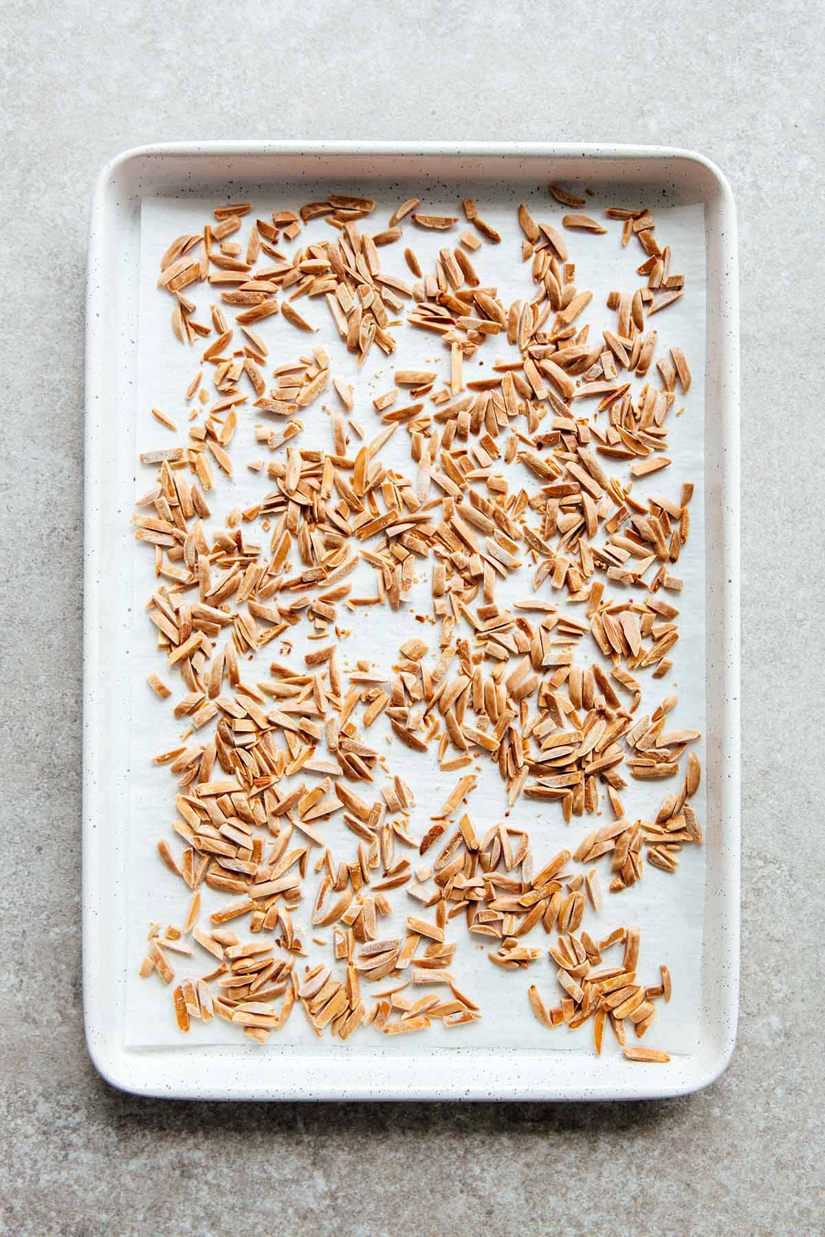Toasted slivered almonds on a parchment paper-lined white baking sheet.