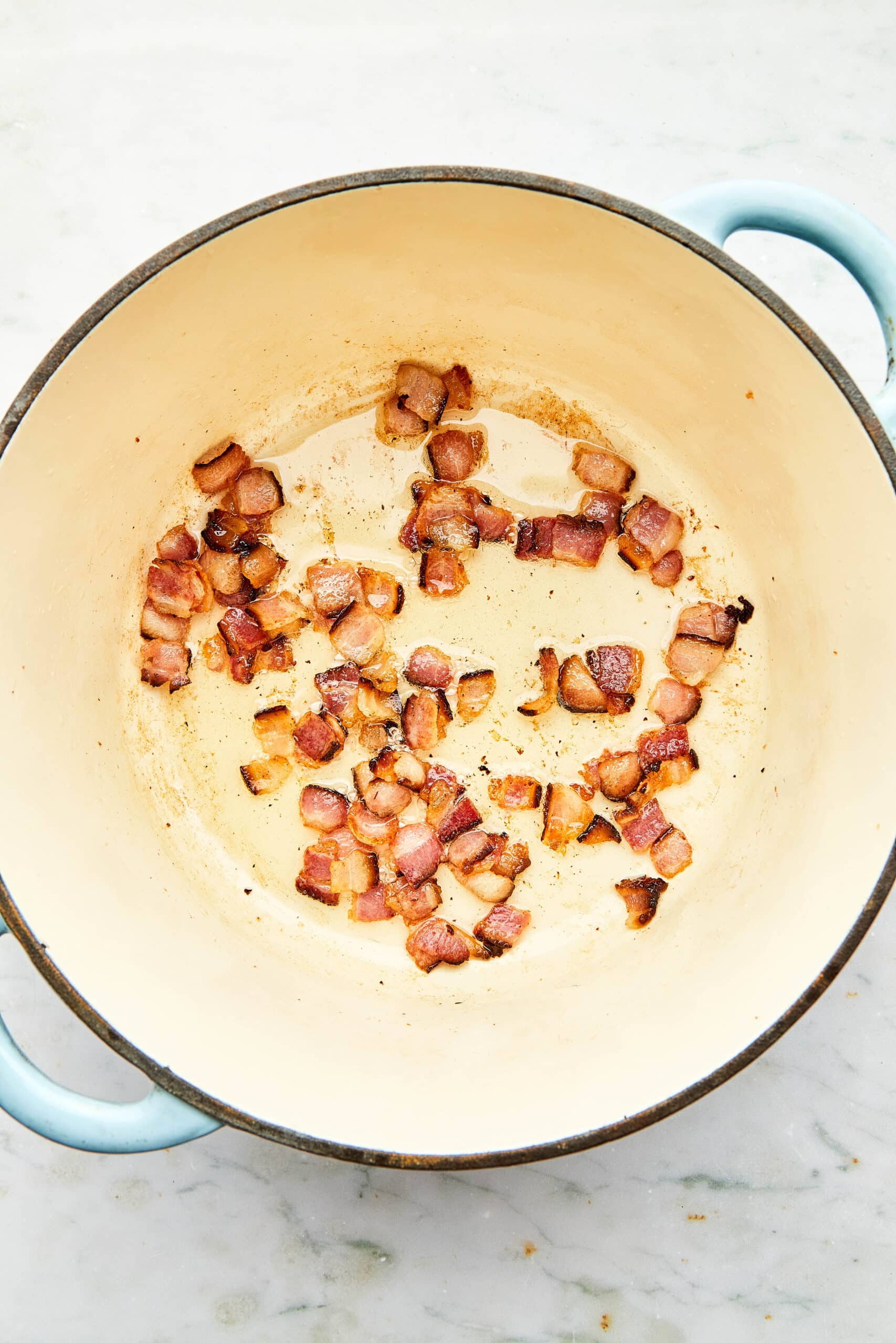 Chopped bacon cooking in a cast iron pot.