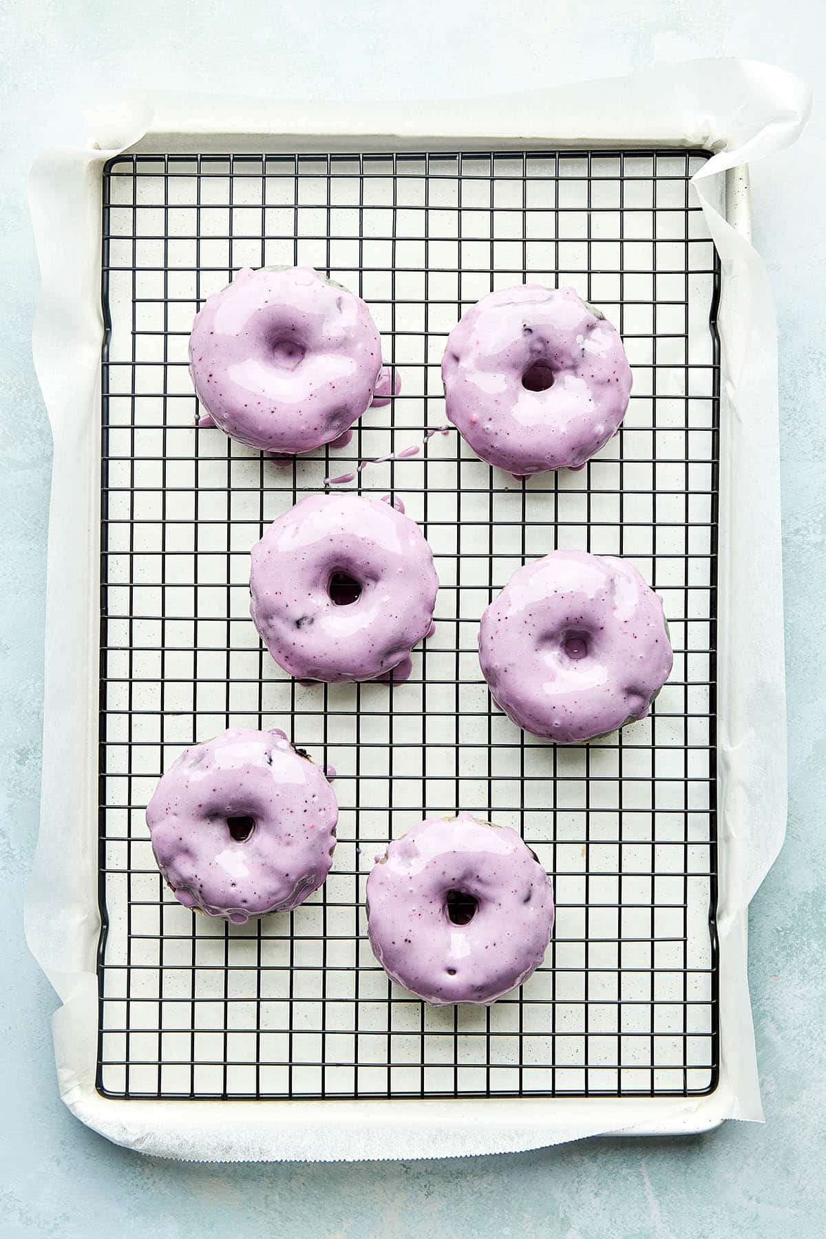 Baked blueberry donuts cooling on a wire rack set inside a parchment lined baking sheet.