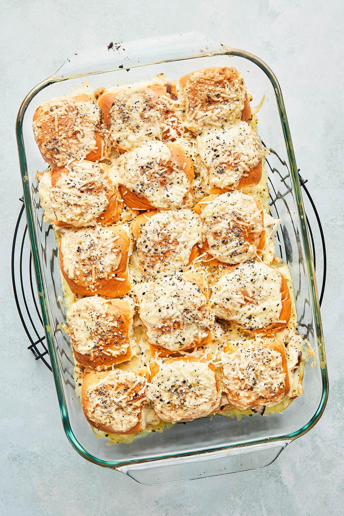 A rectangle baking dish of sweet Hawaiian roll sandwiches on a wire rack.