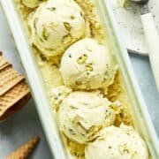 A tub of homemade pistachio ice cream with five scoops of the ice cream sitting on top.