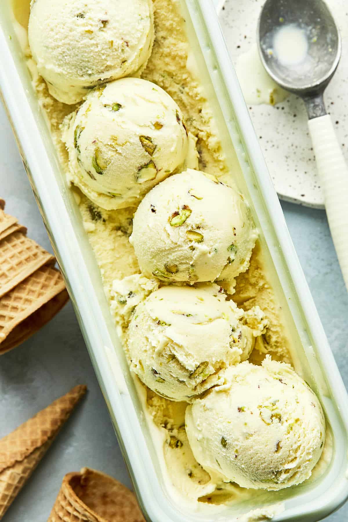 A tub of homemade pistachio ice cream with five scoops of the ice cream sitting on top.