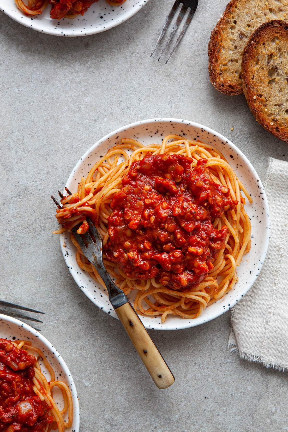 Three plates of spaghetti topped with sauce with toasted bread nearby.