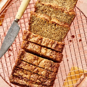 A fully baked and sliced quick bread loaf on a copper cooling rock with linens and a small knife nearby.