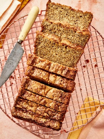 A fully baked and sliced quick bread loaf on a copper cooling rock with linens and a small knife nearby.