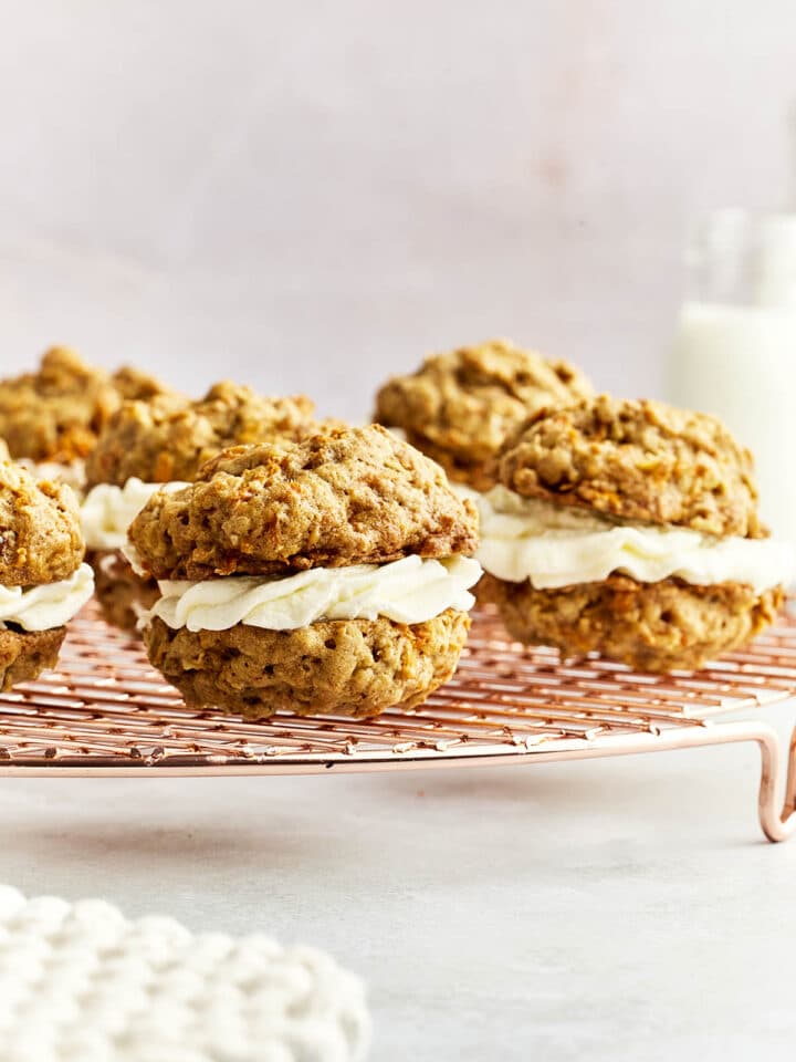 Carrot cake cookies with cream cheese filling on a wire rack with a bottle of milk in the background.