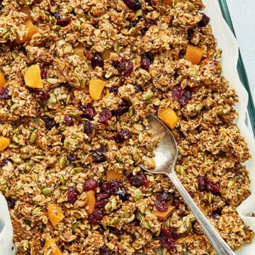 A batch of nut free granola and a baking dish lined with parchment paper with a spoon inside the dish.