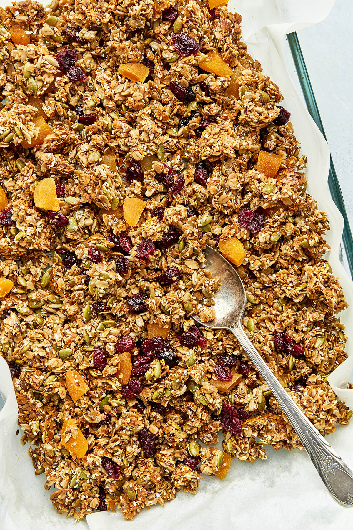 A batch of nut free granola and a baking dish lined with parchment paper with a spoon inside the dish.