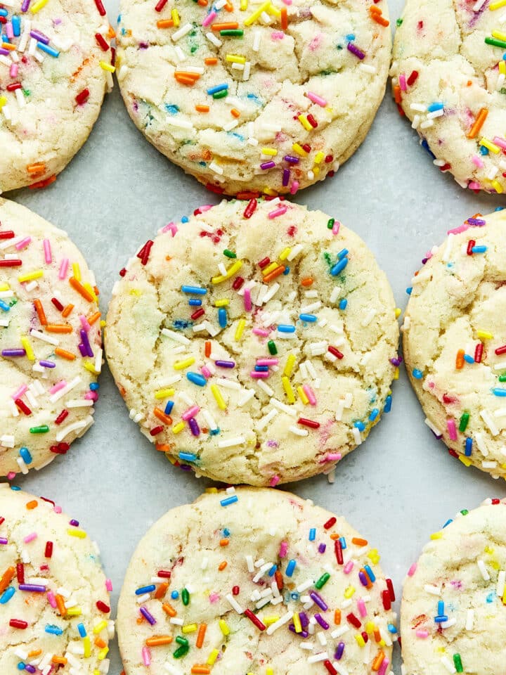 Rainbow sprinkles cookies lined up on a light blueish green surface.