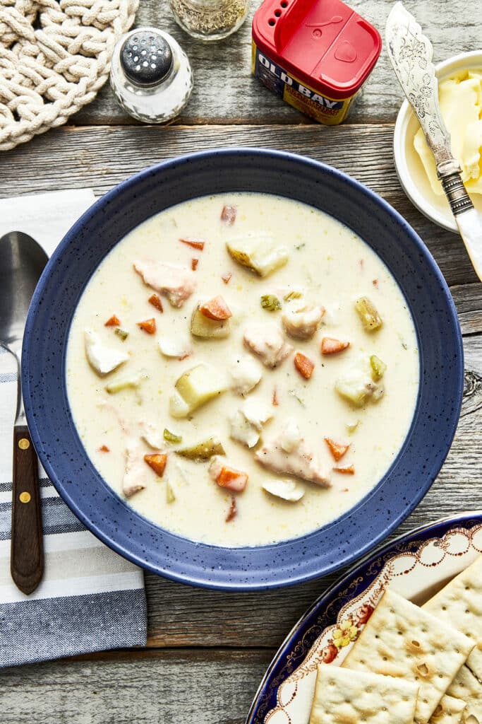 A bowl of Maritime fish chowder on a table with salt and pepper, butter, and Premium Plus crackers.