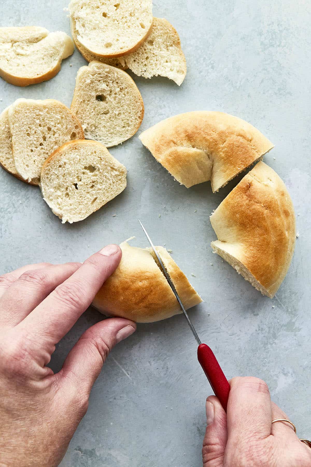 Hands using a small red knife to slice a bagel.