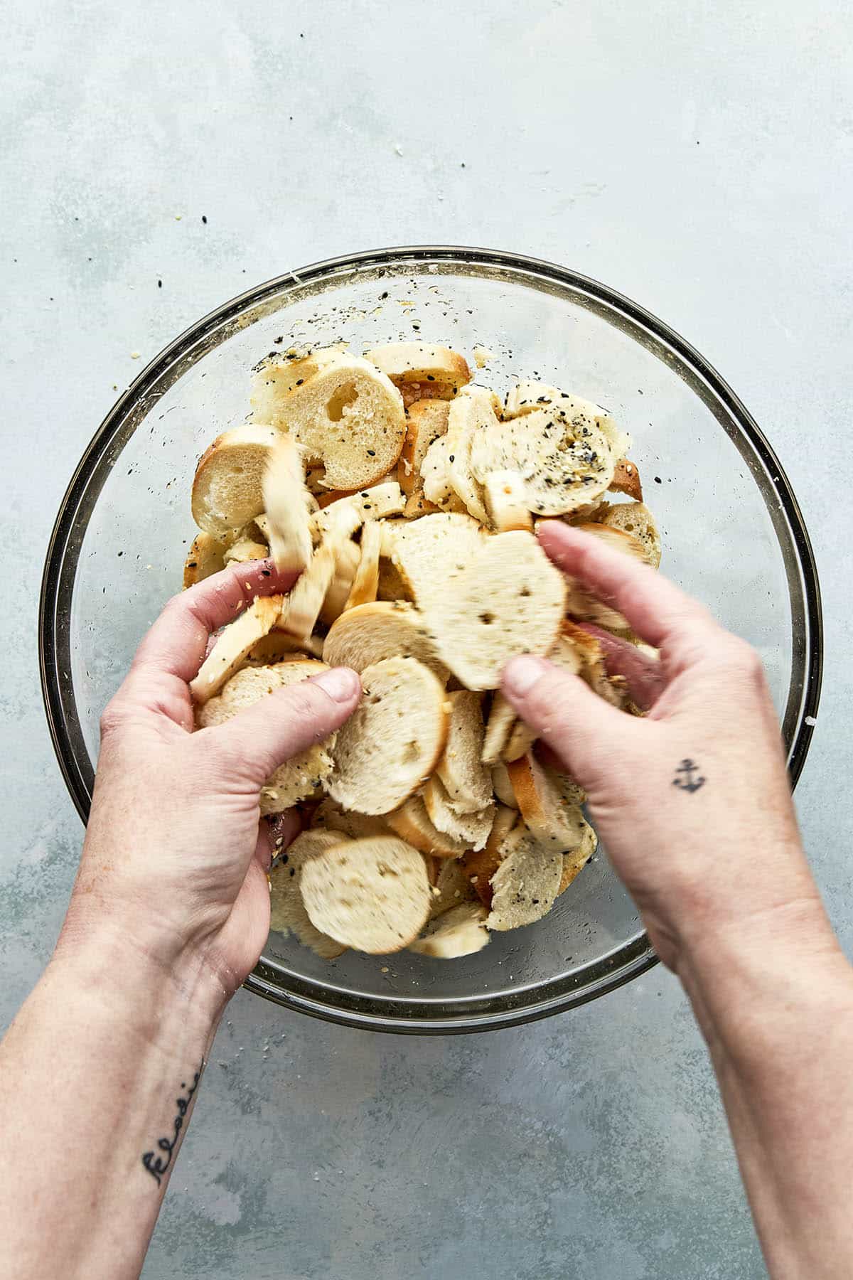 Hands tossing sliced bread pieces in a large bowl.