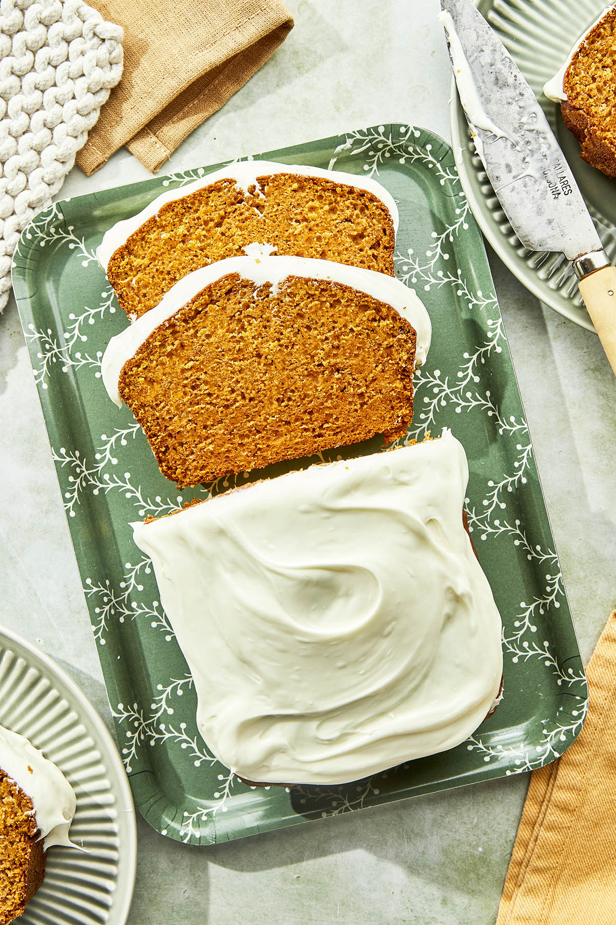 Pumpkin bread with cream cheese frosting on a green decorative tray with two slices showing.