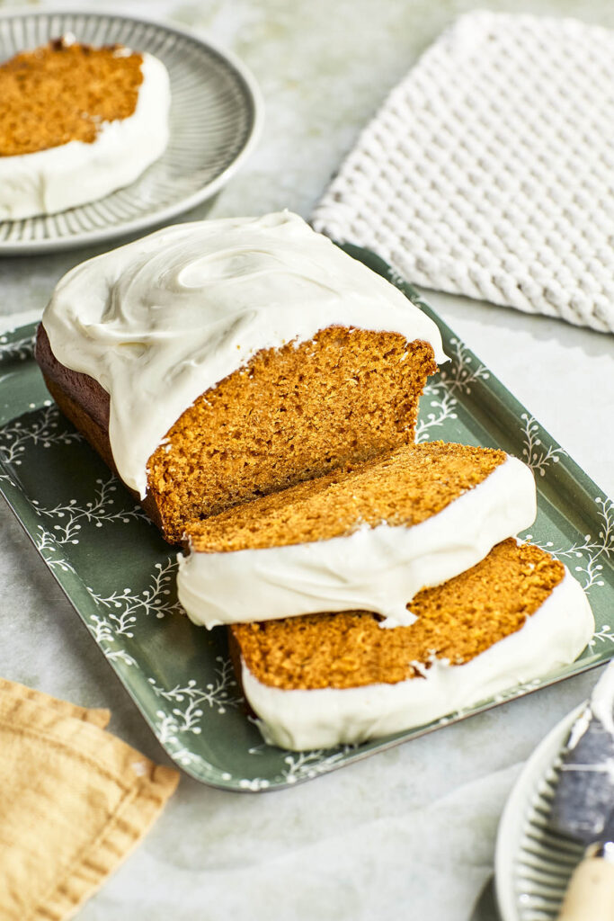 A 45° view of a sliced pumpkin loaf with cream cheese frosting.