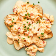 Creamed lobster on a slice of buttered toast, topped with chives on a green plate.