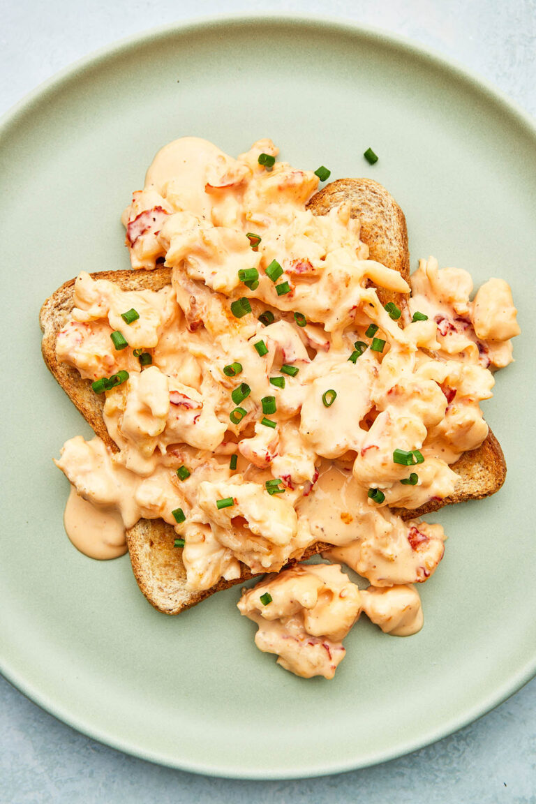Creamed lobster on a slice of buttered toast, topped with chives on a green plate.