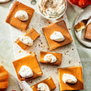 Pumpkin pie bars on a terrazzo serving board topped with whipped cream.