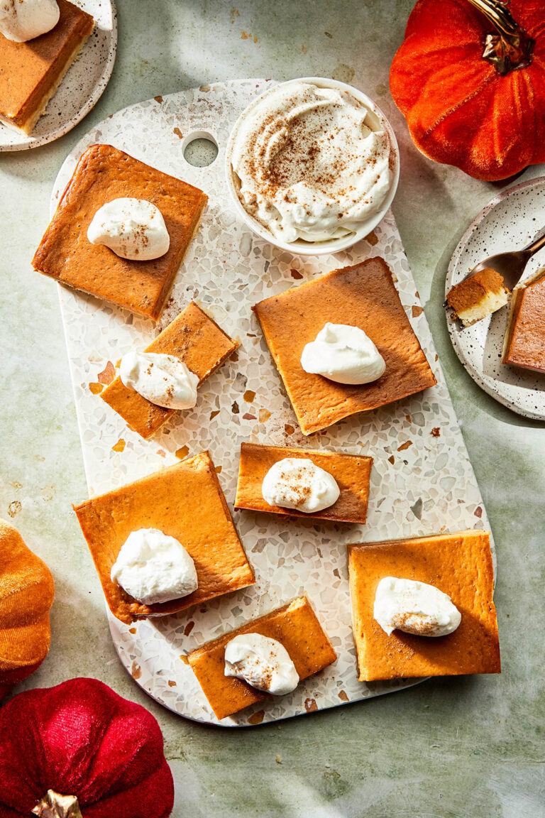 Pumpkin pie bars on a terrazzo serving board topped with whipped cream.