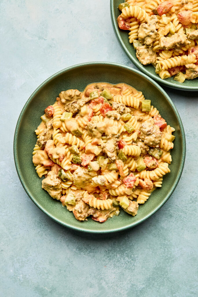 Two green bowls of cheeseburger pasta on a blueish-greenish background.