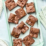 A pan of double chocolate chip cookie bars with plates and linens nearby.